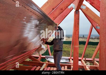 L'operatore isola la soffitta della casa con un film di hydrofilm, assicura l'isolamento con l'aiuto di una graffatrice.2020 Foto Stock