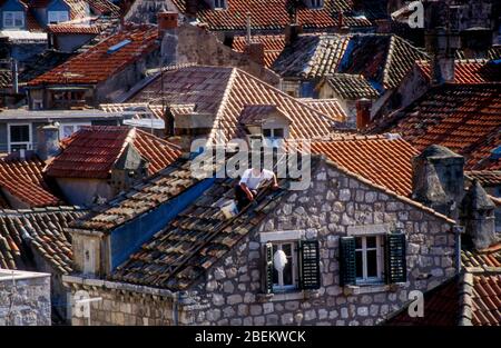 1994 Dubrovnik, Croazia - uomo che ripara il tetto danneggiato da bombardamenti nel centro storico della città, raffigurato durante un gabbiamento in bombardamenti da parte dell'esercito serbo Foto Stock