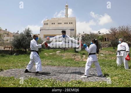 Hebron. 14 Aprile 2020. L'istruttore palestinese di Karate Sami al-Jabaa (R) si allena con i suoi familiari che indossano maschere facciali a causa del COVID-19, nel giardino della loro casa nella città di Hebron della Cisgiordania il 14 aprile 2020. Credit: Mamoun Wazwaz/Xinhua/Alamy Live News Foto Stock