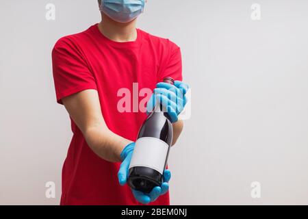 Uomo che indossa guanti protettivi e maschera che tiene una bottiglia di vino Foto Stock
