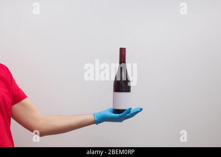 Uomo che indossa guanti protettivi e maschera che tiene una bottiglia di vino Foto Stock