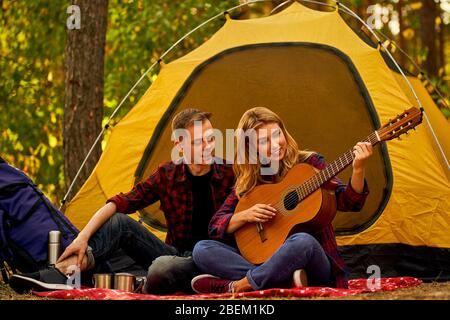 Campeggio nella foresta. Coppia in amore felice rilassante natura sfondo. Chitarra fidanzata vicino alla tenda da campeggio. Aria fresca e sensazioni pure. Campin Foto Stock