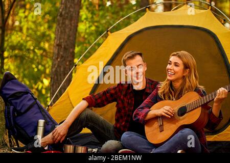 Campeggio nella foresta. Coppia in amore felice rilassante natura sfondo. Chitarra fidanzata vicino alla tenda da campeggio. Aria fresca e sensazioni pure. Campin Foto Stock