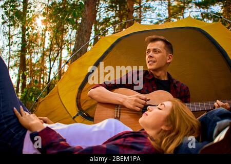 Campeggio nella foresta. Coppia in amore felice rilassante natura sfondo. Chitarra fidanzata vicino alla tenda da campeggio. Aria fresca e sensazioni pure. Campin Foto Stock