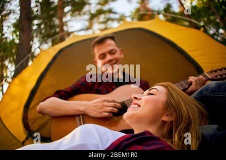 Campeggio nella foresta. Coppia in amore felice rilassante natura sfondo. Chitarra fidanzata vicino alla tenda da campeggio. Aria fresca e sensazioni pure. Campin Foto Stock