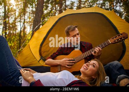 Campeggio nella foresta. Coppia in amore felice rilassante natura sfondo. Chitarra fidanzata vicino alla tenda da campeggio. Aria fresca e sensazioni pure. Campin Foto Stock