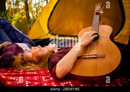 Campeggio nella foresta. Coppia in amore felice rilassante natura sfondo. Chitarra fidanzata vicino alla tenda da campeggio. Aria fresca e sensazioni pure. Campin Foto Stock