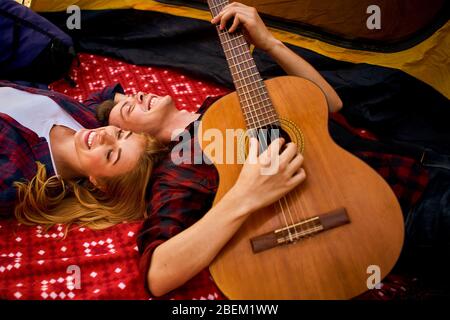 Campeggio nella foresta. Coppia in amore felice rilassante natura sfondo. Chitarra fidanzata vicino alla tenda da campeggio. Aria fresca e sensazioni pure. Campin Foto Stock