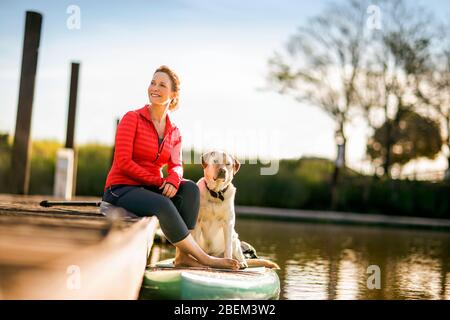 Donna di mezza età adulta seduta su un molo con il suo cane Foto Stock