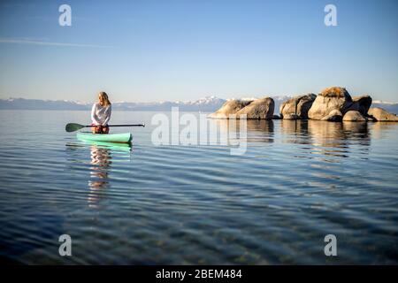 Giovane donna attiva pagaia a bordo attraverso un lago Foto Stock