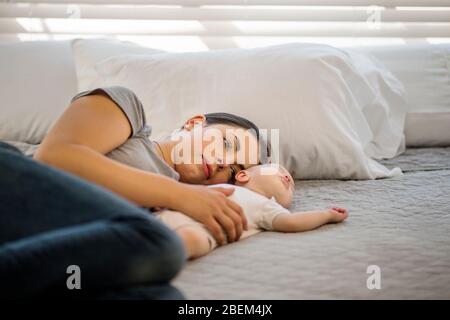 Madre adulta media sdraiata su un letto con il suo bambino addormentato Foto Stock