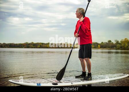 Uomo anziano in piedi su una tavola a paddle su un lago Foto Stock