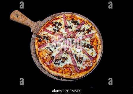 una pizza al prosciutto e ai funghi appena sfornati servita su un piatto di legno Foto Stock