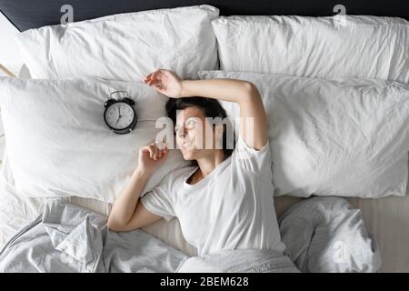 Vista dall'alto. La ragazza dorme accanto alla sveglia. Tentativo di disattivare la sveglia che interferisce con la modalità di sospensione. Tempo di attivazione. Profondo Foto Stock