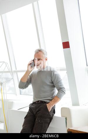 Immagine di un uomo d'affari anziano barbuto grigio-capelli che parla al chiuso da telefono cellulare. Foto Stock