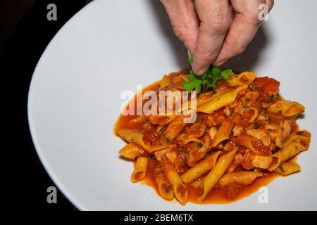 aggiungere il prezzemolo finale guarnire ad un piatto di pasta di pollo arrabiata piccante appena fatto Foto Stock