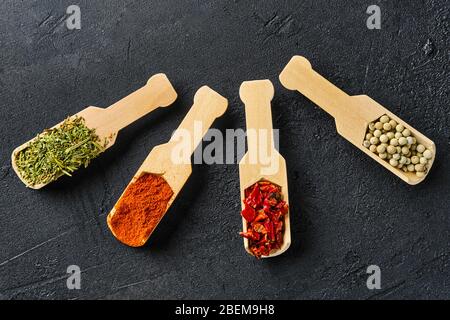 Quattro cucchiai di legno con spezie su fondo di cemento nero Foto Stock