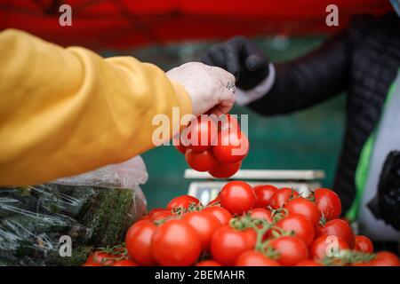 Immagine di profondità di campo (fuoco selettivo) poco profonda con la mano di una vecchia donna che acquista pomodori da una bancarella di verdure. Foto Stock