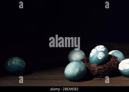 Uova dipinte blu con stampa di prezzemolo in nido su tavola di legno. Decorazione di Pasqua. Vista dall'alto sfondo rustico Foto Stock