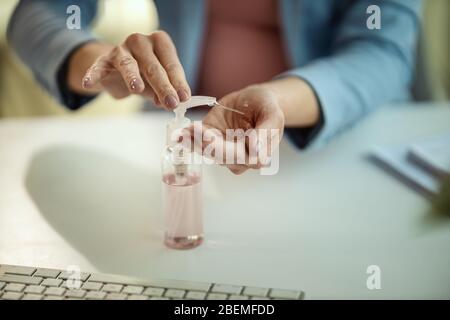 Primo piano di una donna d'affari irriconoscibile utilizza gel antisettico antibatterico per la disinfezione delle mani in un luogo di lavoro durante l'autoisolamento e quaran Foto Stock