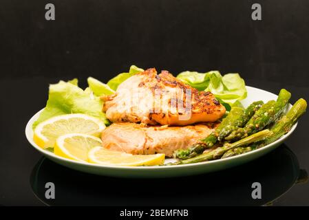 Piatto con salmone alla griglia e asparagi su sfondo nero Foto Stock