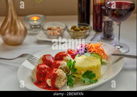 Deliziose polpette di carne su piatto caldo servite con purè di patate. Bicchiere di vino rosso, olive, mandorle sullo sfondo, primo piano. Foto Stock