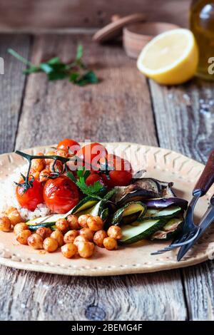 Piatto a base di piante vegane, ciotola con quinoa, ceci, zucchine alla griglia, melanzane, pomodori in ciotola ceramica su un tavolo rustico in legno, lifesyl sostenibile Foto Stock