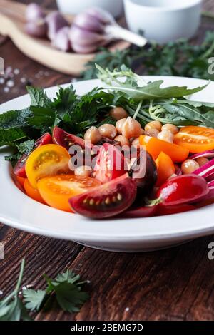 Piatto a base di piante vegane, ciotola con ceci, pomodori freschi e colorati, ravanello affettato, cetrioli, erbe in ceramica su un tavolo rustico in legno, sostenibile Foto Stock