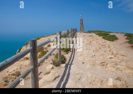 Portogallo, Cabo da Roca, il Capo Roca occidentale d'Europa, sentieri escursionistici sul Capo Roca, corrimano in legno sulla strada di pietra, una croce sulla cima di Foto Stock