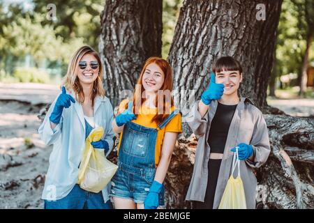 Amici che raccolgono rifiuti dal parco. Le ragazze mostrano il pollice in su. Foto Stock