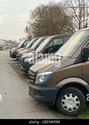 Immagine verticale fila di furgoni marroni per la consegna dei trasporti parcheggiati di fronte all'edificio del magazzino con cielo drammatico - logistica moderna per il settore dell'e-commerce Foto Stock