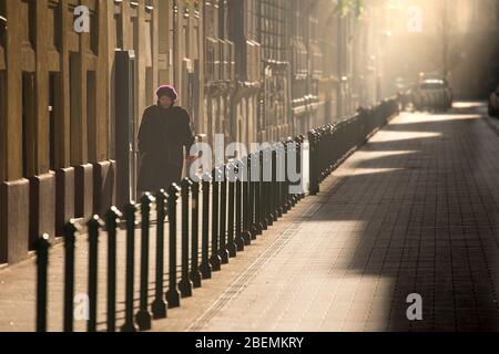 Una pedone femminile che cammina su un marciapiede alla luce del mattino presto, Budapest Foto Stock