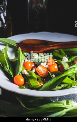 Insalata fresca con aglio selvatico, pomodori e formaggio feta sul piatto. Ramsons lascia. Foto Stock