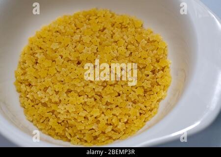 Un piccolo piatto bianco in ceramica contiene pasta stelline secca e cruda. Questa variante più piccola della pasta di zuppa di stelle ha la forma di piccole stelle. Foto Stock