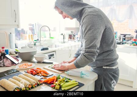 Giovane uomo caucasico che fa sushi a casa dopo la cucina video lezioni online sul sito web via smartphone. Tecnologia Internet per lo stile di vita moderno co Foto Stock