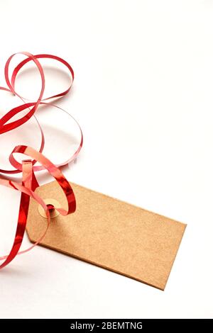 Etichetta regalo marrone vuota con nastro rosso arricciato. Etichetta di cartone Kraft isolata su sfondo bianco. Shopping, vendita, celebrazione o natale concetto. Foto Stock