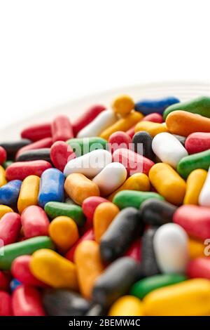 Primo piano di caramelle dolci colorate e lucide in blu, rosso, giallo, verde, nero e bianche su piattino. Verticale con angolo olandese con spazio di copia. Foto Stock