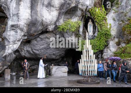 Pellegrini in visita alla Grotta delle Massabielle mentre un sacerdote cattolico celebra la messa a Lourdes, Francia, Europa Foto Stock