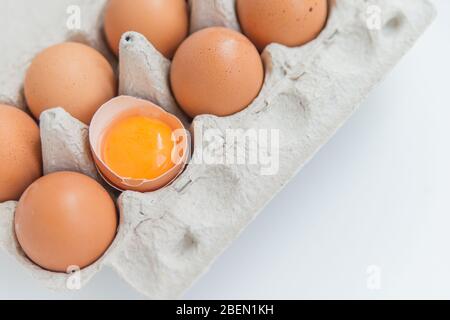 Primo piano del pacchetto di dieci uova brune e un uovo rotto sul bianco Foto Stock