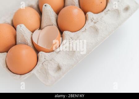 Primo piano del pacchetto di dieci uova brune e un uovo rotto sul bianco Foto Stock