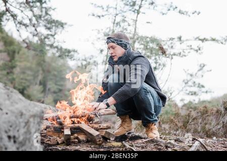 Uomo che mette bastoni su un fuoco all'aperto in Svezia Foto Stock