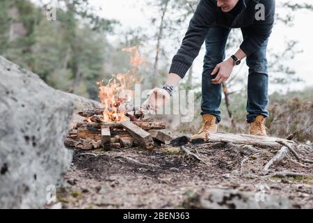 Uomo che mette bastoni su un fuoco all'aperto in Svezia Foto Stock