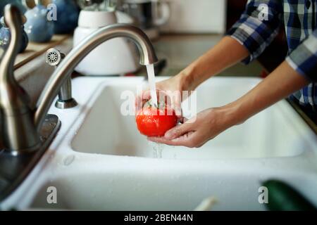 Primo piano delle mani della donna che lavano un tomatoe Foto Stock