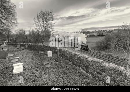 West Coast Railways 8F locomotiva a vapore passando il cimitero a Bentham con un treno speciale Santa mainline a vapore charter. Foto Stock