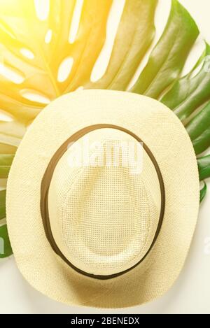 Accessori da viaggio. Cappello di paglia e foglia di monstera tropicale su sfondo bianco. Vacanze di viaggio, vivere lentamente, godere di concetto. Sfondo estivo. Disposizione piatta, vista dall'alto. Foto Stock