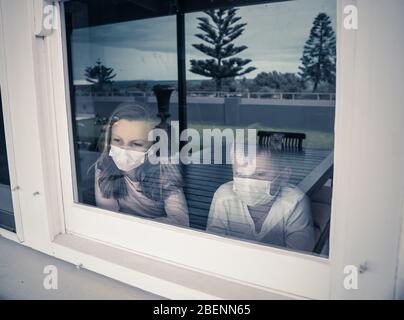 Blocchi COVID-19. Bambini tristi con maschera facciale che guarda attraverso la finestra durante la quarantena a casa. I bambini si sentono tristi quando la scuola è chiusa. Coronaviru Foto Stock