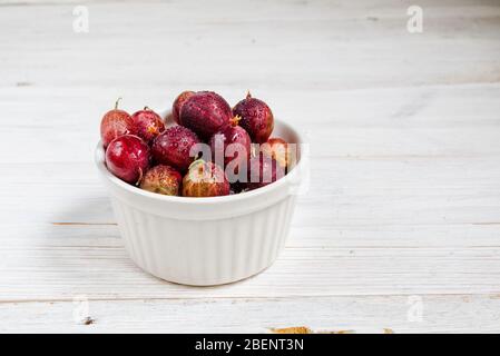 Set di uva spina biologica. Frutti di bosco in una tazza. Rosso di uva spina su sfondo rustico di legno. Frutti di bosco dolci e succosi. Vista dall'alto. Foto Stock