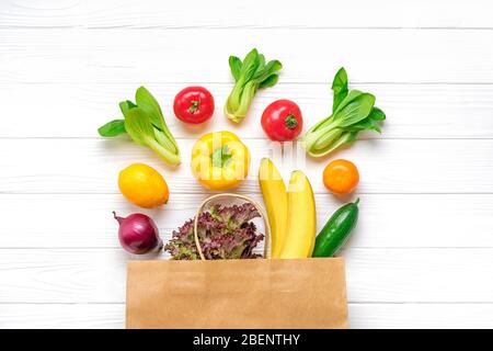 Sacchetto di carta eco-completa di diversi alimenti per la salute - peperone giallo, pomodori, banane, lattuga, verde, cetriolo, cipolle su sfondo di legno bianco Top v Foto Stock