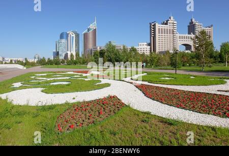 NUR-Sultan, ASTANA, KAZAKHSTAN - 3 GIUGNO 2015: Vista della città sul letto fiorito con ornamento di fiori di petunia con edifici skyscapper e KazMunaygas Foto Stock