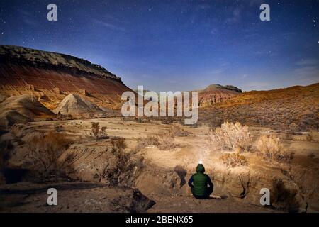 Uomo con luce di testa seduto per terra nel deserto di notte sullo sfondo del cielo. Viaggi, avventuri e concetto di spedizione. Foto Stock